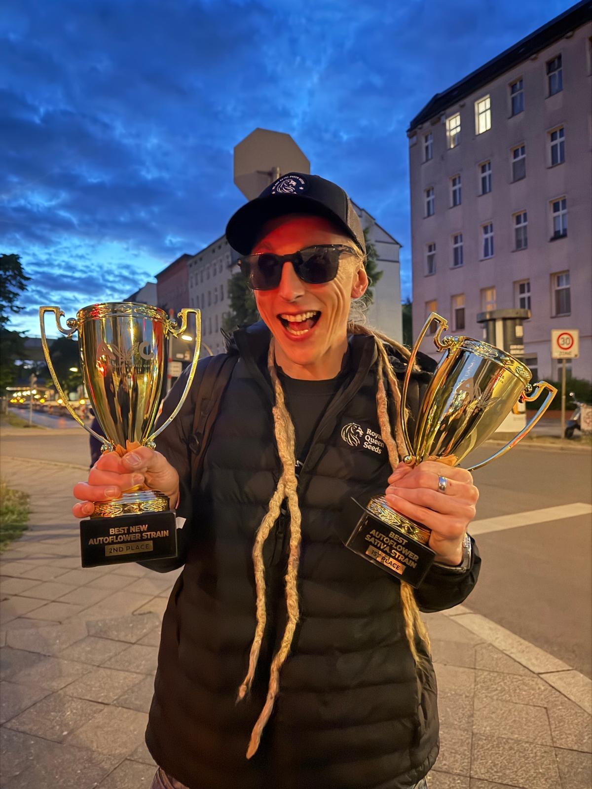 Max from Royal Queen Seeds holding the two Autoflower World Cup 2026 trophies outdoors in Berlin at dusk